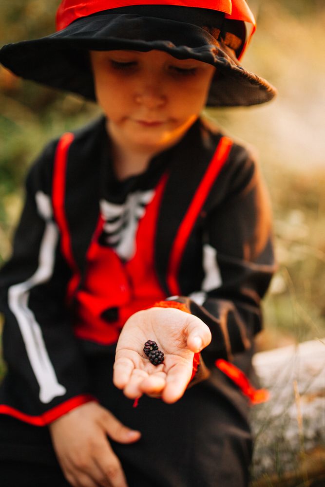 Boy in skeleton costume looking down at berries in his hand