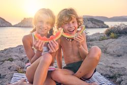 Happy brother and sister with watermelon slices at seaside