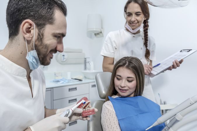 Smiling male dentist showing dental jaw model to female patient