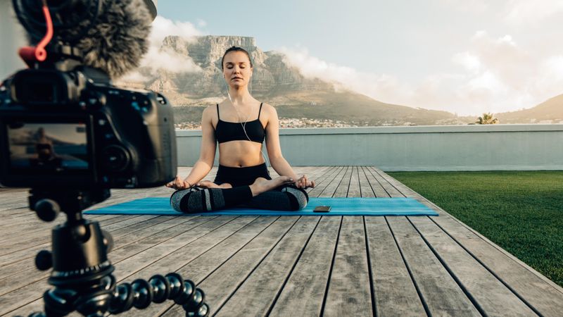 Camera mounted on flexible tripod recording a fitness woman meditating in a yoga posture