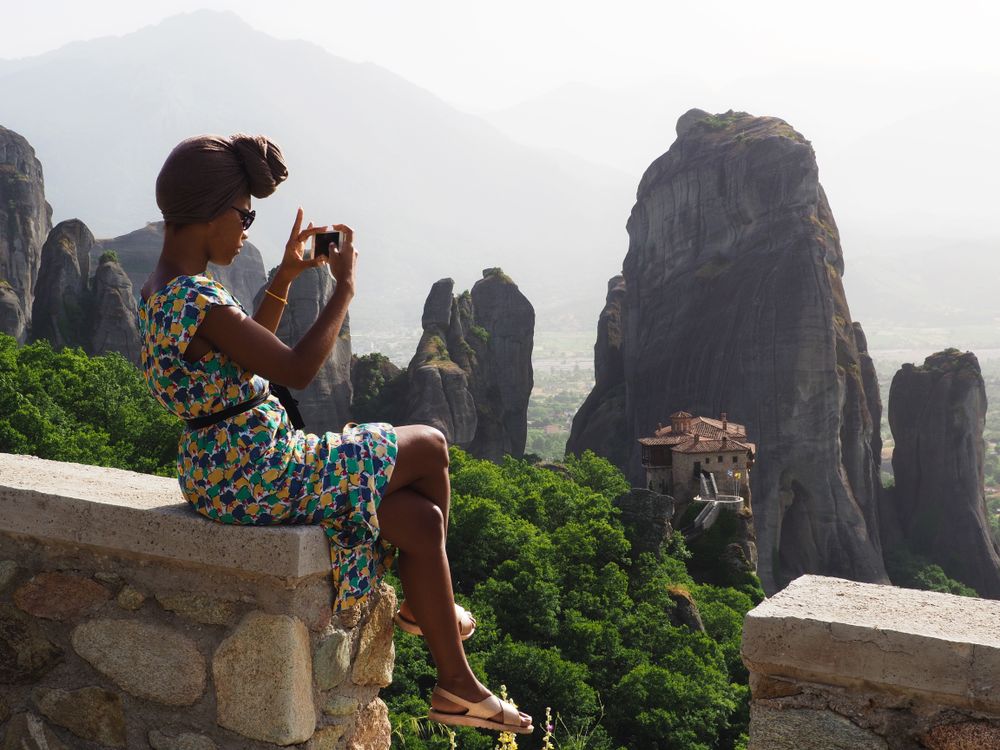 Woman in blue and yellow floral dress taking photo of mountain