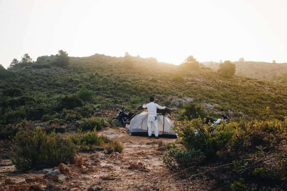 Man setting up a tent in a field with parked motorcycle