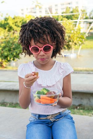 Little girl eating healthy food in a park. Family lifestyle concept.