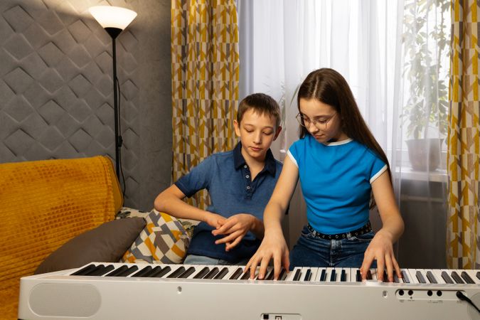 Girl teaches boy to play digital piano at home.