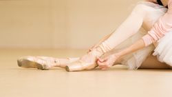 Ballet dancer tying ribbons on pointe shoes