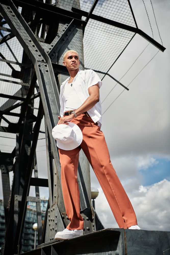 Stylish young man holding hat on bridge