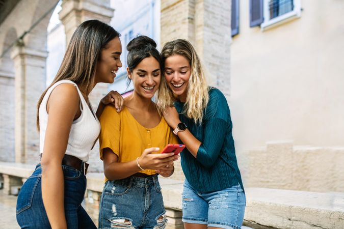 Three female friends looking down and smiling at friends phone