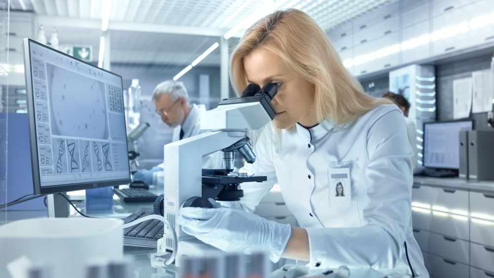 Female Research Scientist Looks at Biological Samples Under Microscope.