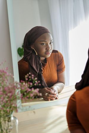 Pensive Black female in hijab looking in mirror