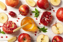 Looking down at fall fruit of pomegranates and apples with pot of honey on wooden table, close up