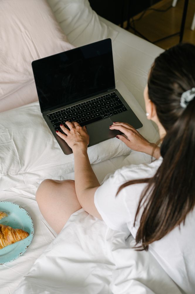 Crop woman using laptop on bed having breakfast