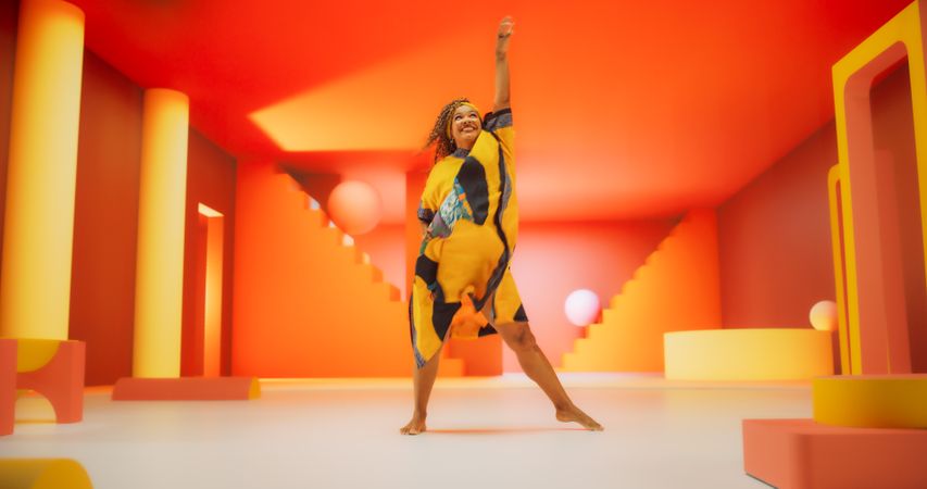 Black Woman in African Outfit Dancing Energetically in Geometric Abstract Orange Environment. Creative Female Performing Dance Choreography in Bright Studio, Making Moves, Having Fun.