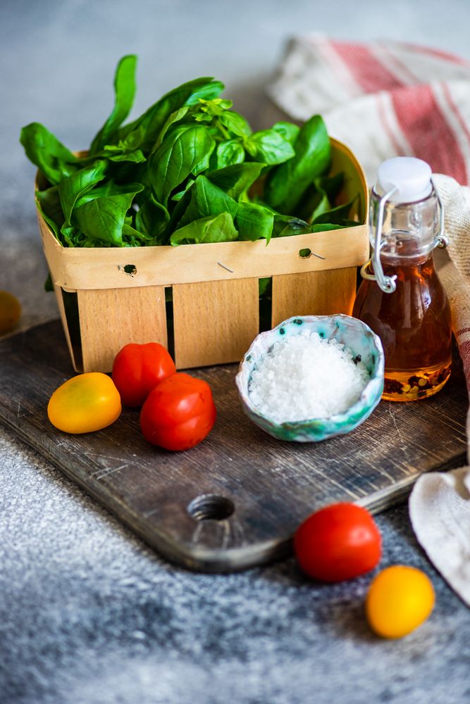 Fresh basil, cherry tomatoes, salt and oil on bread board on kitchen counter