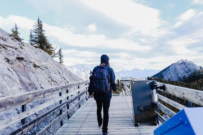 Back view of young woman with backpack walking on wooden bridge in the mountains
