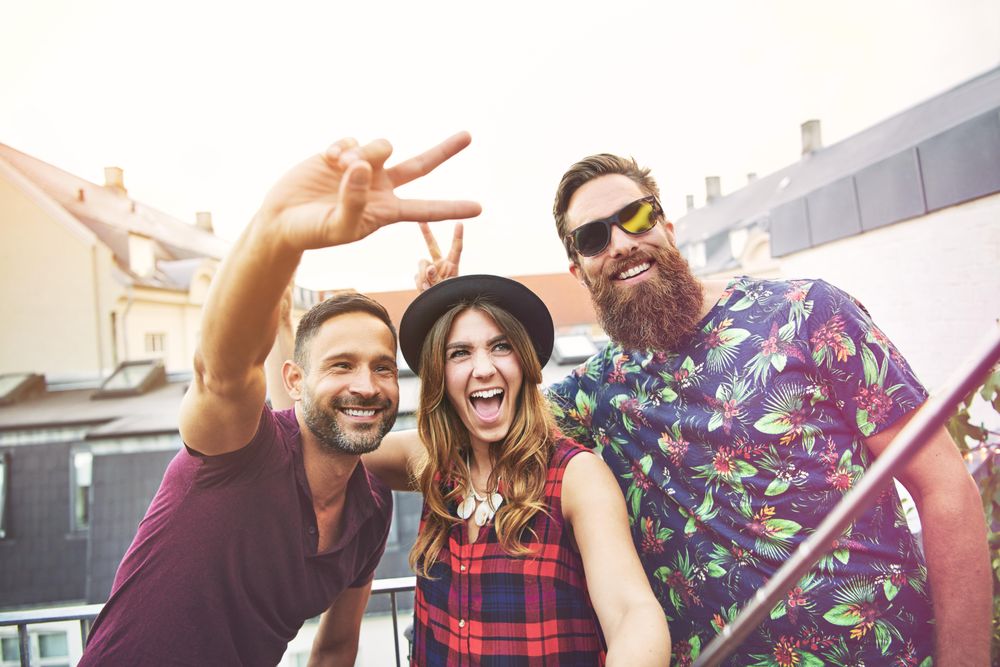 Three smiling friends making peace signs and goofy rabbit ears taking selfie