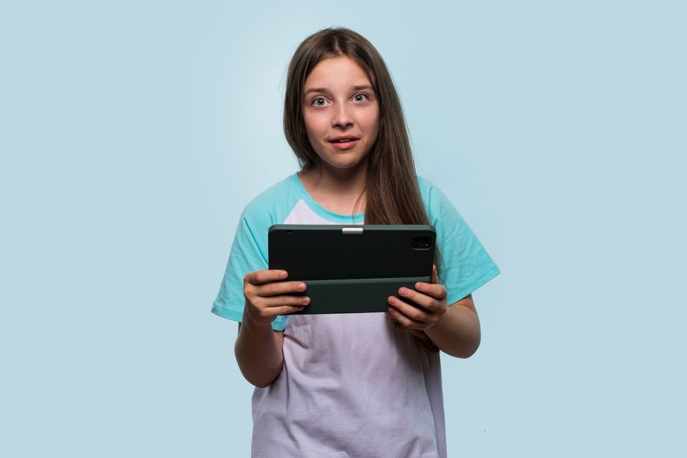Surprised young girl holding tablet, showing shocked expression.