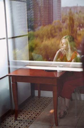 Young adult woman sitting at the table and working on laptop