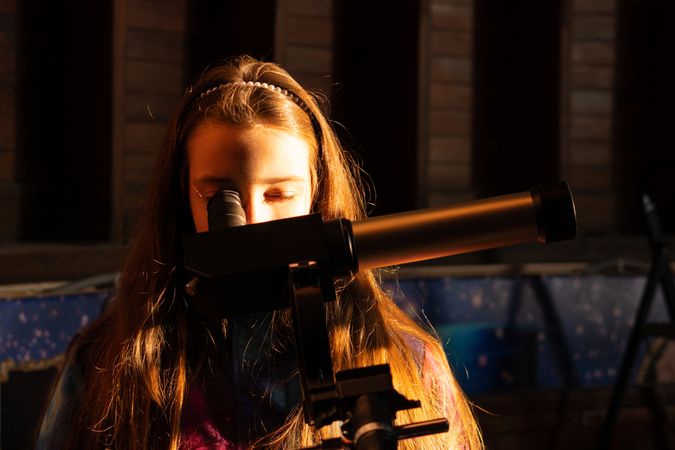 Girl with long hair studies sky through solar telescope.