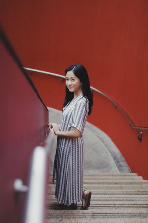 Woman in light and blue dress standing on stairs near red wall