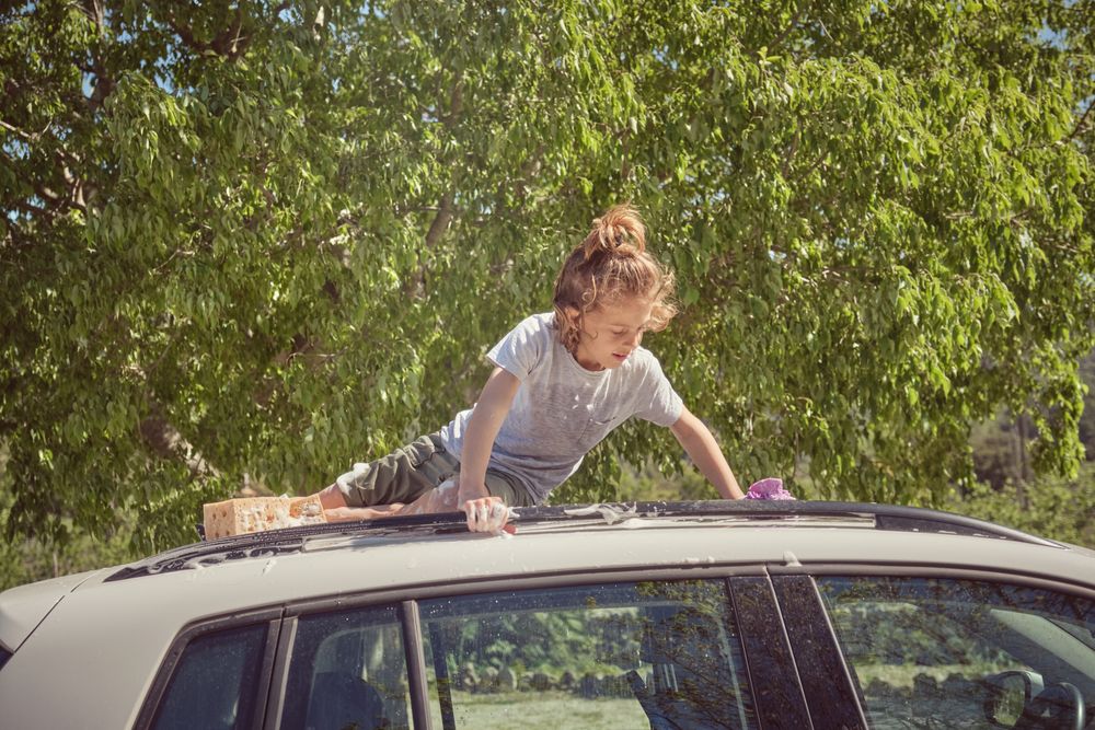 Attentive kid washing automobile roof in summer