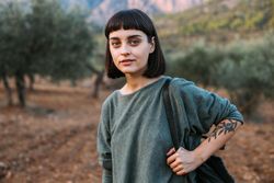 Woman with book bag on shoulder surrounded by trees