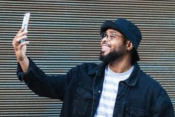 Laughing Black man taking selfie on smartphone