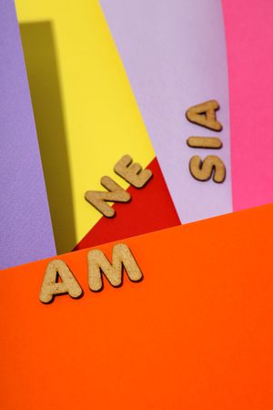 Scattered cork letters spelling “amnesia” on colorful paper background, vertical