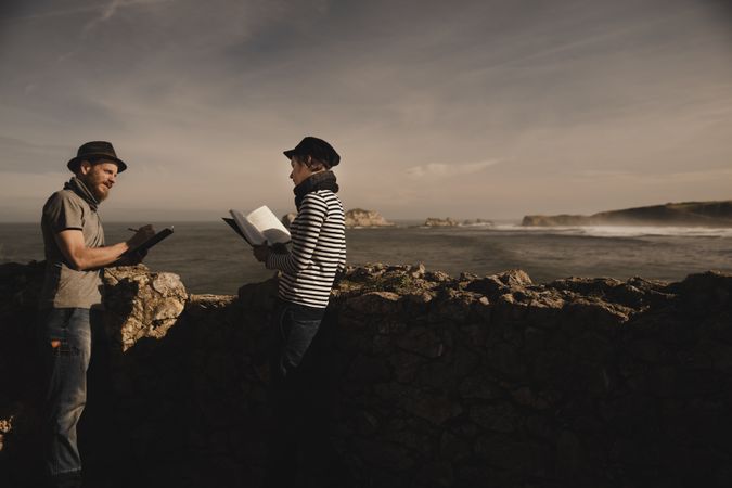 Man near woman with books near stones on shore