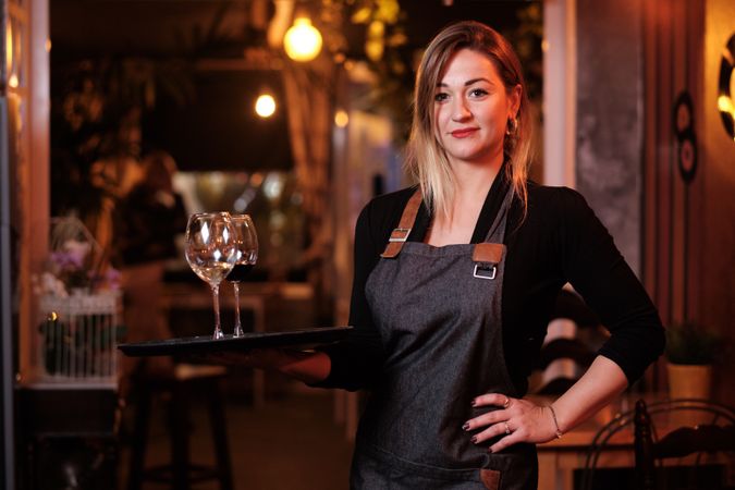 Cheerful waitress holding tray with wineglasses