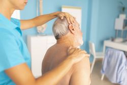 A female physiotherapist performs stretches on the neck of her patient, an older man in rehabilitation