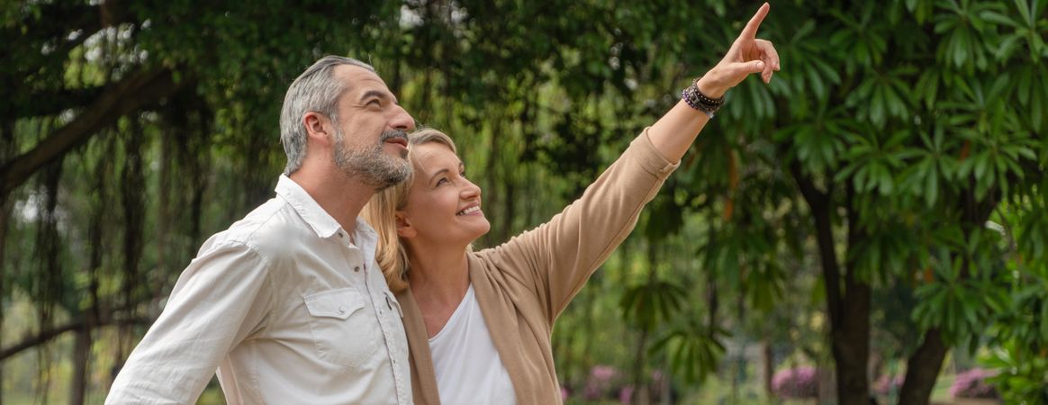 Banner shot of mature man and woman standing in tree filled park and pointing up