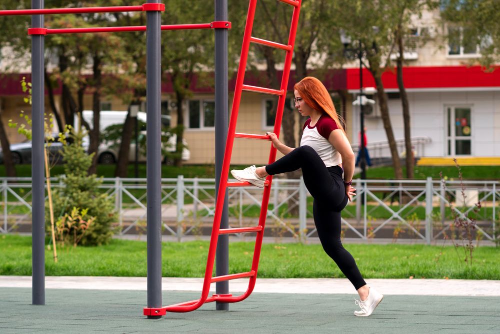 Woman lifting leg on outdoor ladder during workout