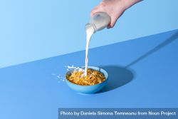 Pouring milk in a cereal bowl on a blue background 4mml74