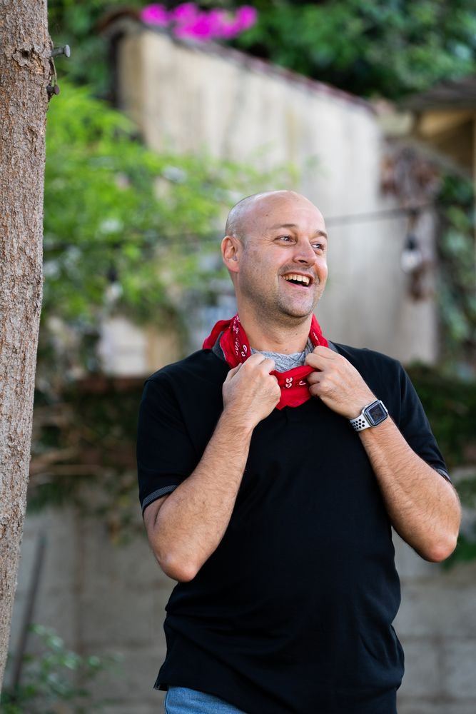 Happy man laughing and looking to the side with his hands holding red bandana around his neck