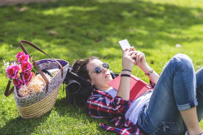 Side view of a hipster happy woman lying on grass in sunny day at park while reading a red book