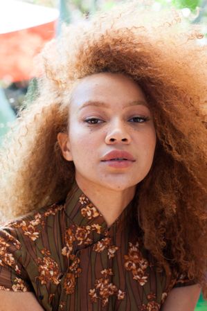 Close up portrait of a young woman outdoors facing the camera with an afro