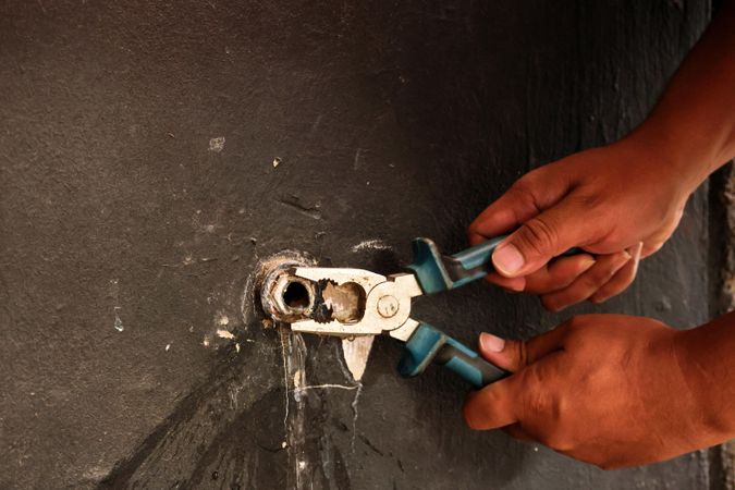 Hand of Asian Plumber Fixing Broken Water Tap on the Wall using Pliers