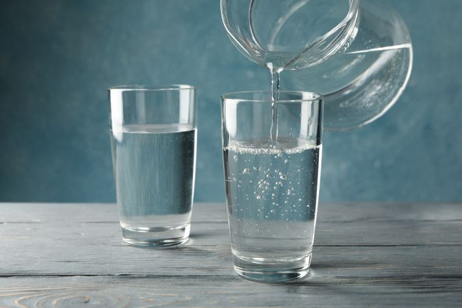 Pitcher of water pouring two glasses of water in blue room