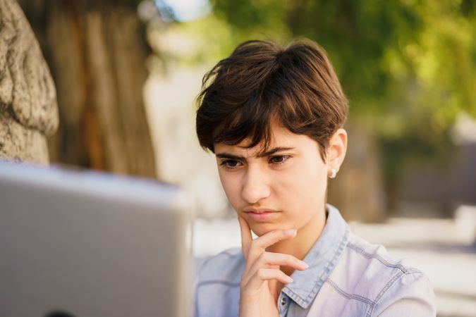 A Thoughtful Young Woman Engaged in Serious Work on Her Laptop in an Outdoor Setting