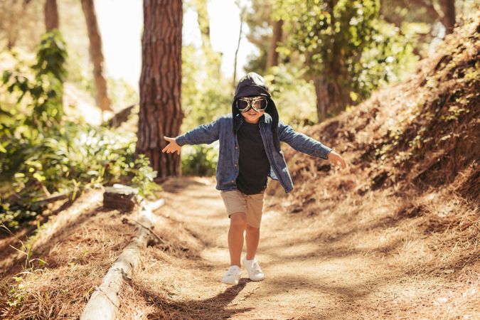Cute boy with pilot goggles and hat running in forest