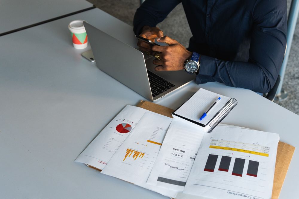 Black man working on laptop with smartphone in office
