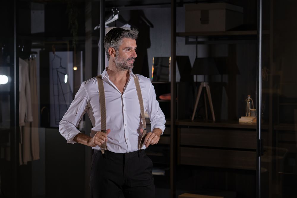 Stylish man standing with hands on suspenders