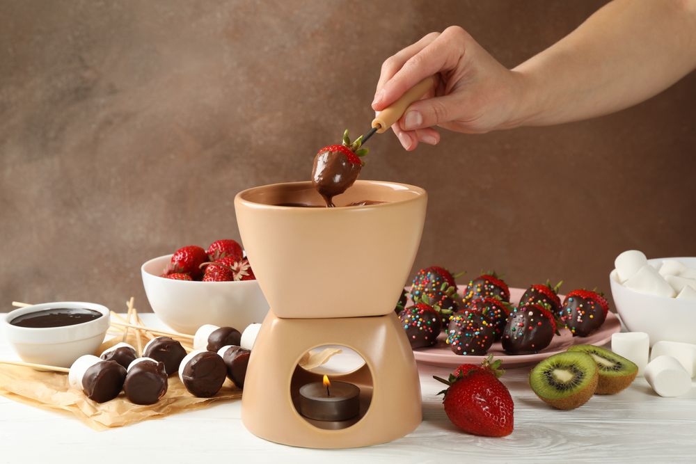 Woman dipping strawberry in chocolate. Delicious chocolate fondue