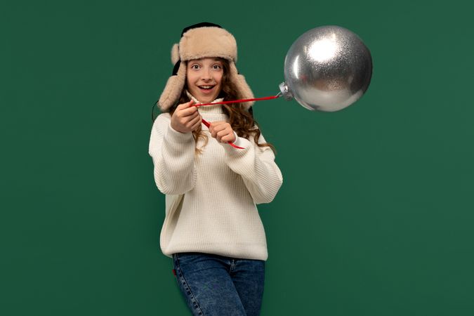 Excited girl swinging large silver ornament with red ribbon.