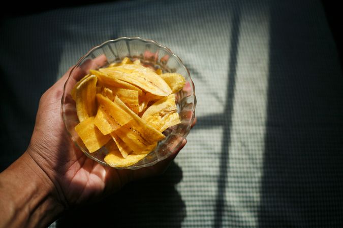 Dried banana slices in bowl in morning light in a person’s hand