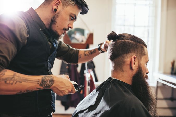 Stylish hairdresser cutting hair of client at barbershop