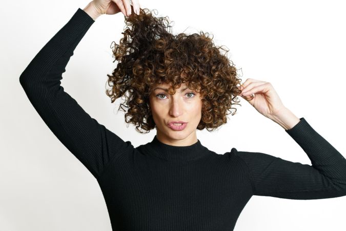 Woman in dark sweater touching her hair with both hands