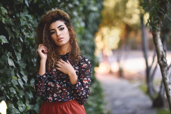 Arab woman wearing casual clothes in the street lined with greenery playing with hair
