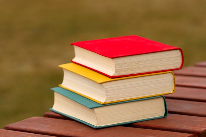 Stack of three colorful hardcover books on wooden bench outdoors.