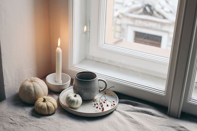 Burning candle, ceramic candleholder by window in moody fall composition